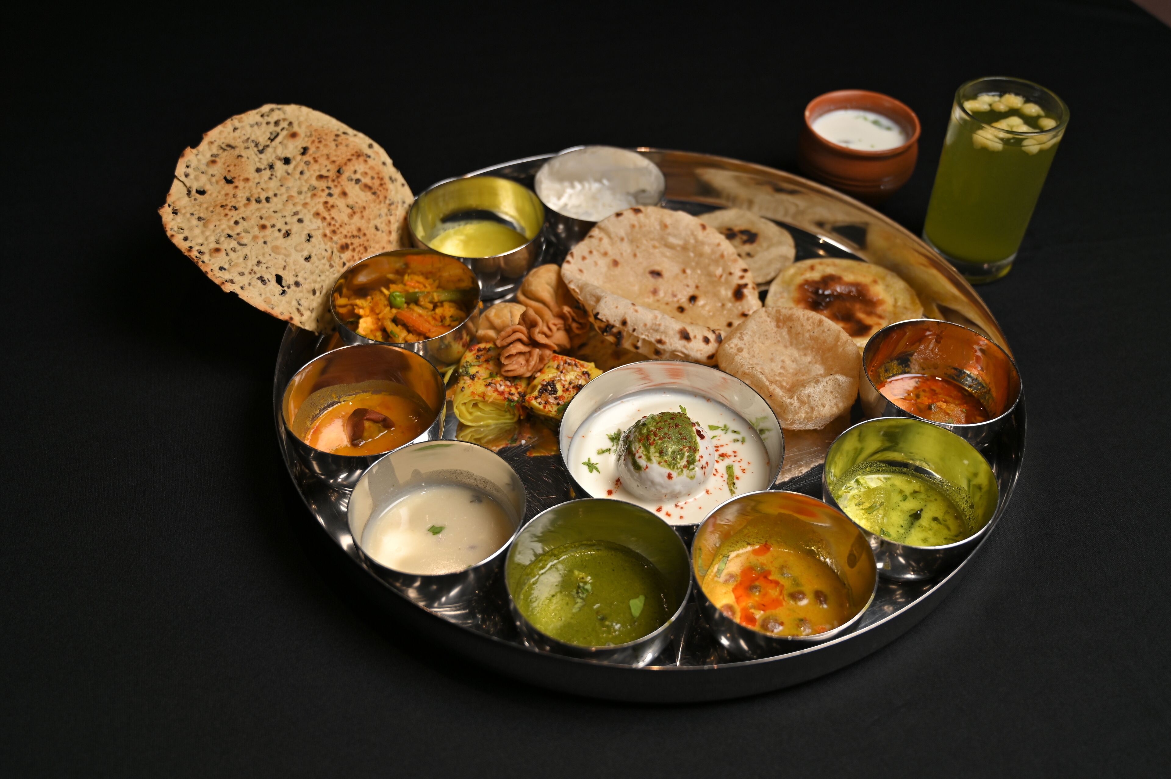 Eine traditionelle indische Mahlzeit mit verschiedenen Gerichten und Chutneys auf einer Metallplatte.
