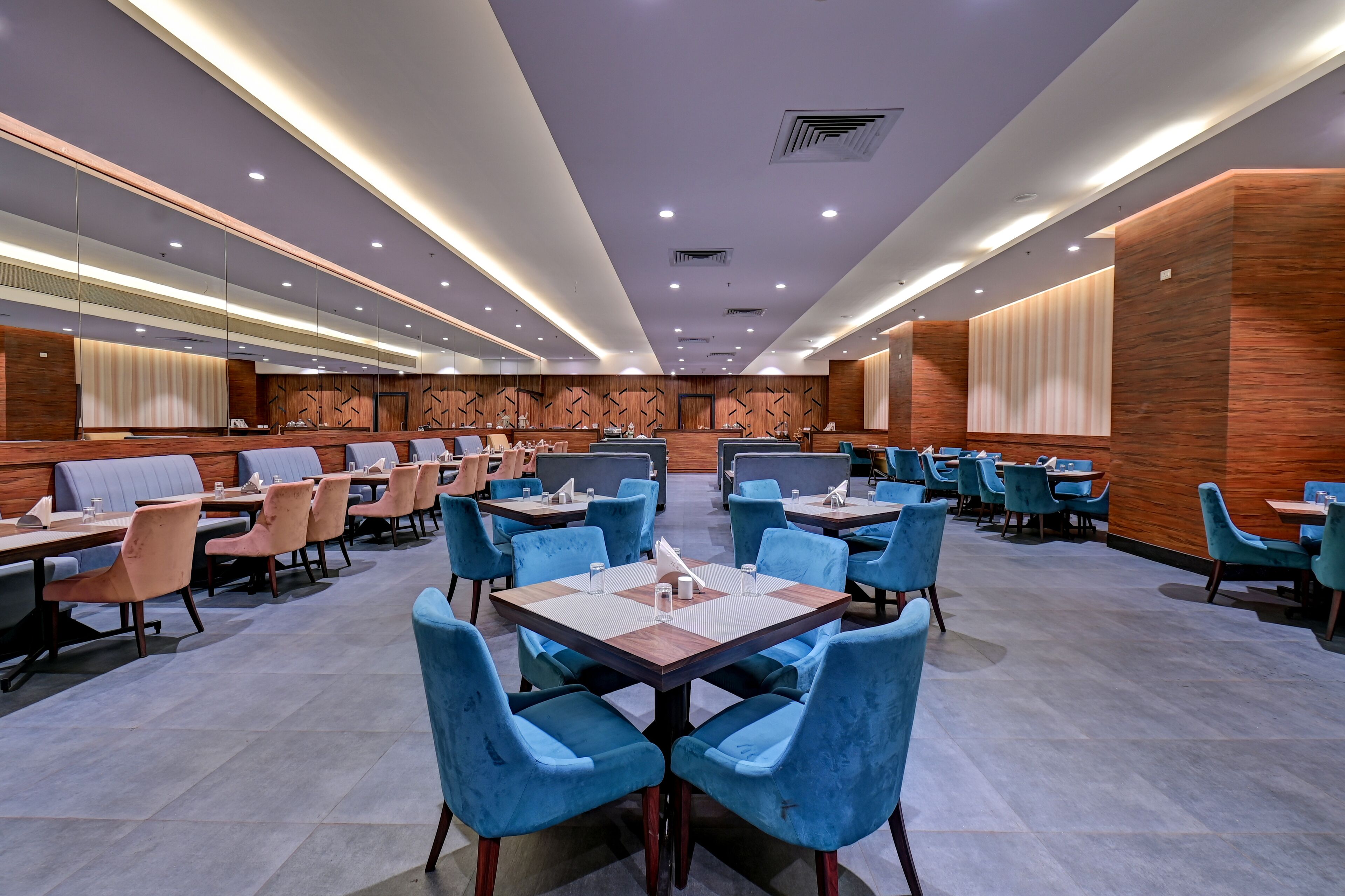 A spacious restaurant with multiple tables and chairs, featuring a modern design with wooden accents and a central seating area.