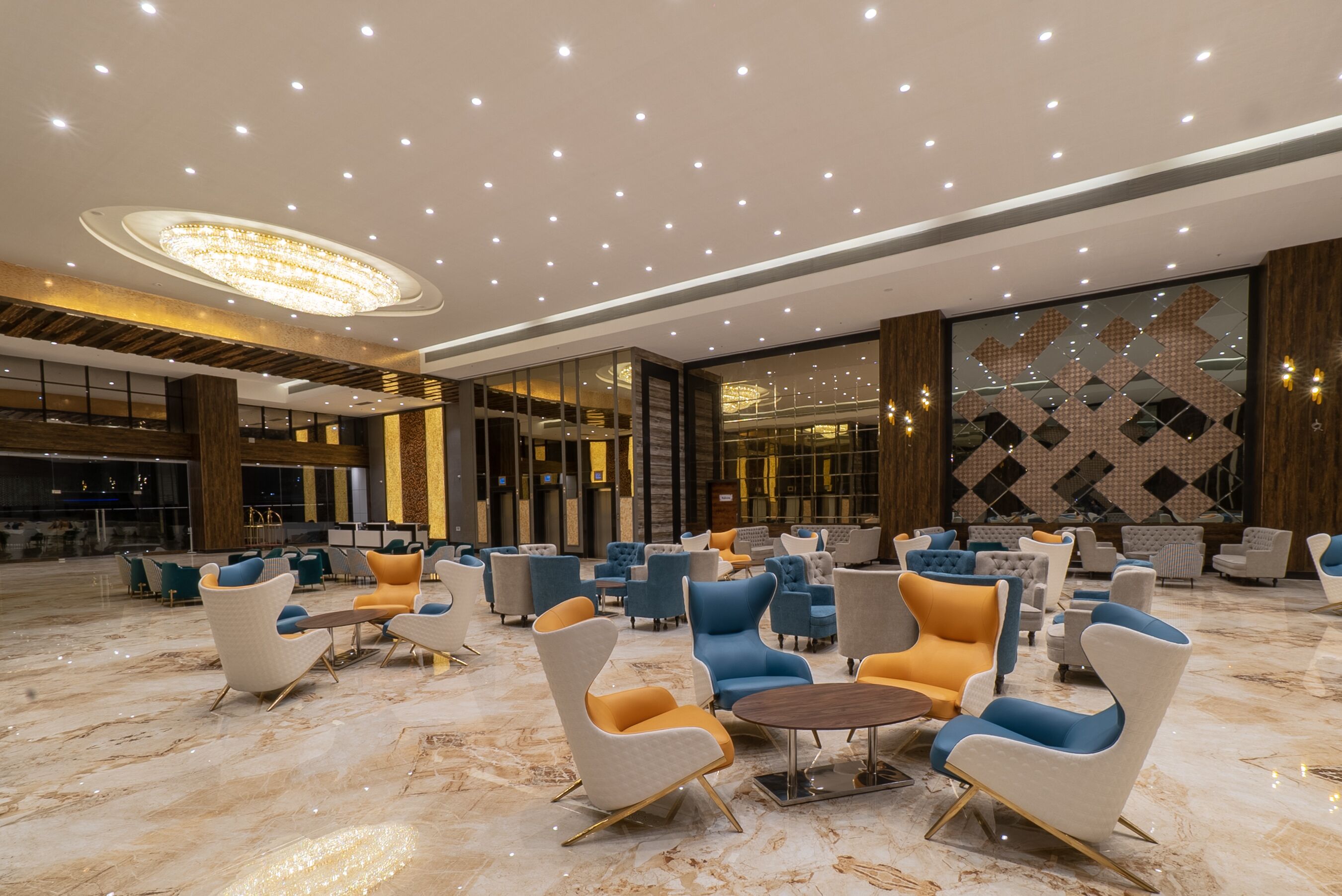 A spacious lobby with modern seating arrangements, a large chandelier, and a patterned wall design.