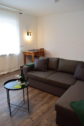 Ein Wohnzimmer mit einer Couch, einem kleinen Tisch mit Flasche und Gläsern, einem Holzesstisch und einer Wandleuchte.