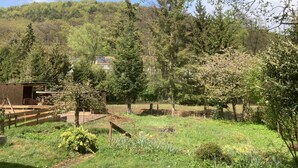 Een landelijk landschap met een houten gebouw, mogelijk een schuur, omringd door bomen en een heuvel op de achtergrond.