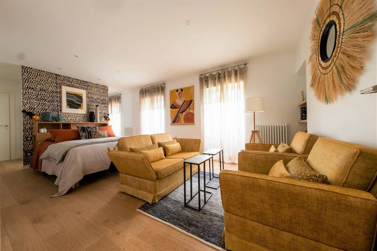 A well-lit room with a bed, two sofas, a small table, and a lamp.