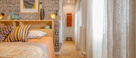 A bedroom with a bed, patterned wallpaper, a framed picture, and a bedside table with a lamp.