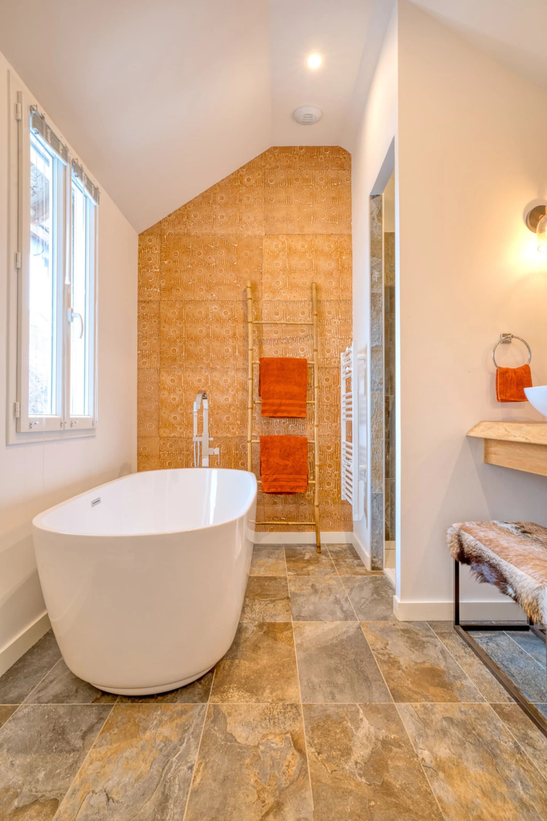 Een moderne badkamer met een vrijstaand bad, een handdoekrek met oranje handdoeken, en een behang met patroon.