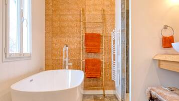 Een moderne badkamer met een vrijstaand bad, een handdoekrek met oranje handdoeken, en een behang met patroon.