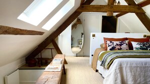 A bedroom with a sloped ceiling, a wooden bench, a bed with multiple pillows, and a mirror on the wall. - Villa Figue Blanche (Montagny-lès-Buxy)