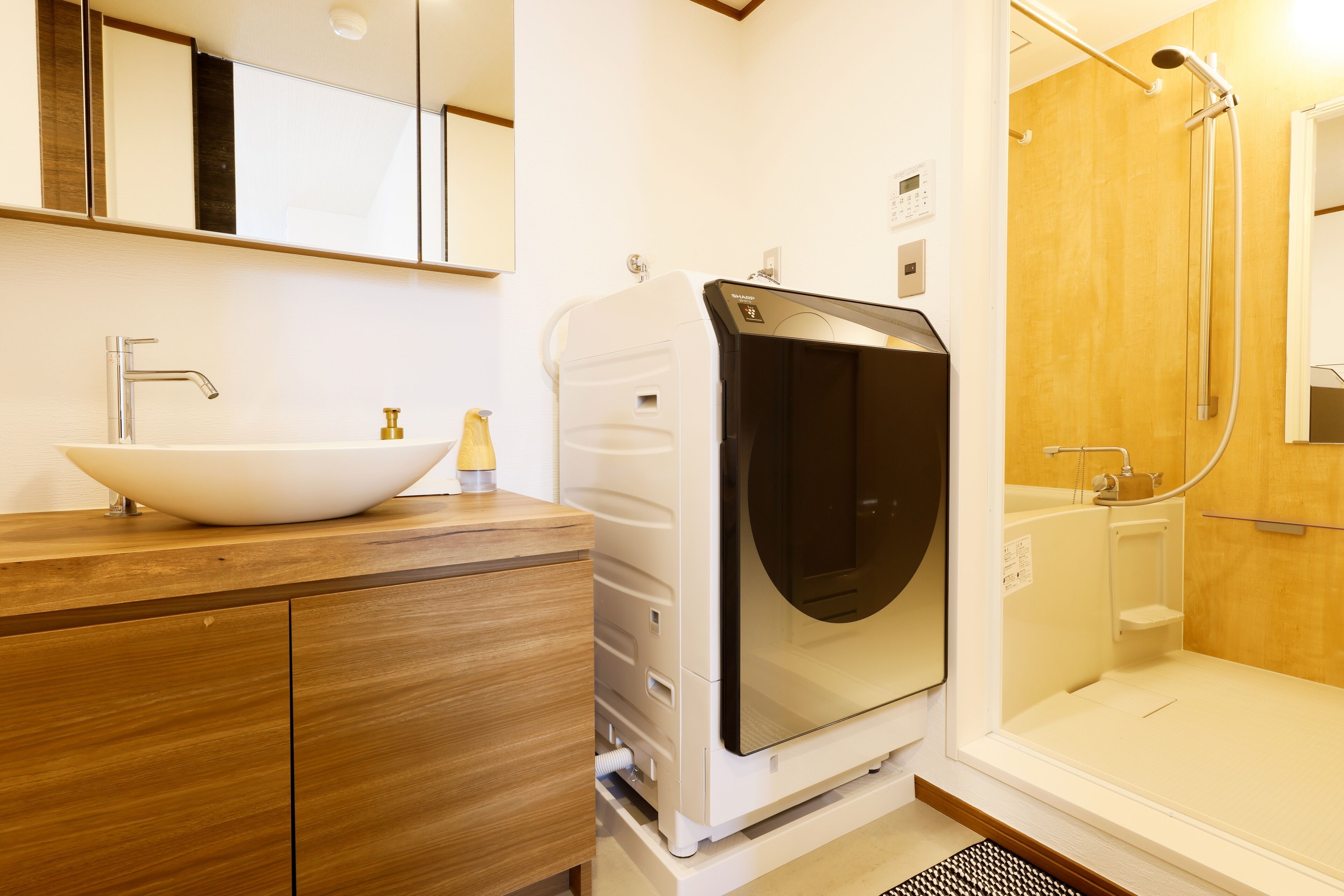 Un baño moderno con un lavabo blanco, tocador de madera y lavadora incorporada.