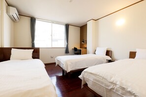 A hotel room with three single beds, a desk, a chair, and a window with curtains.