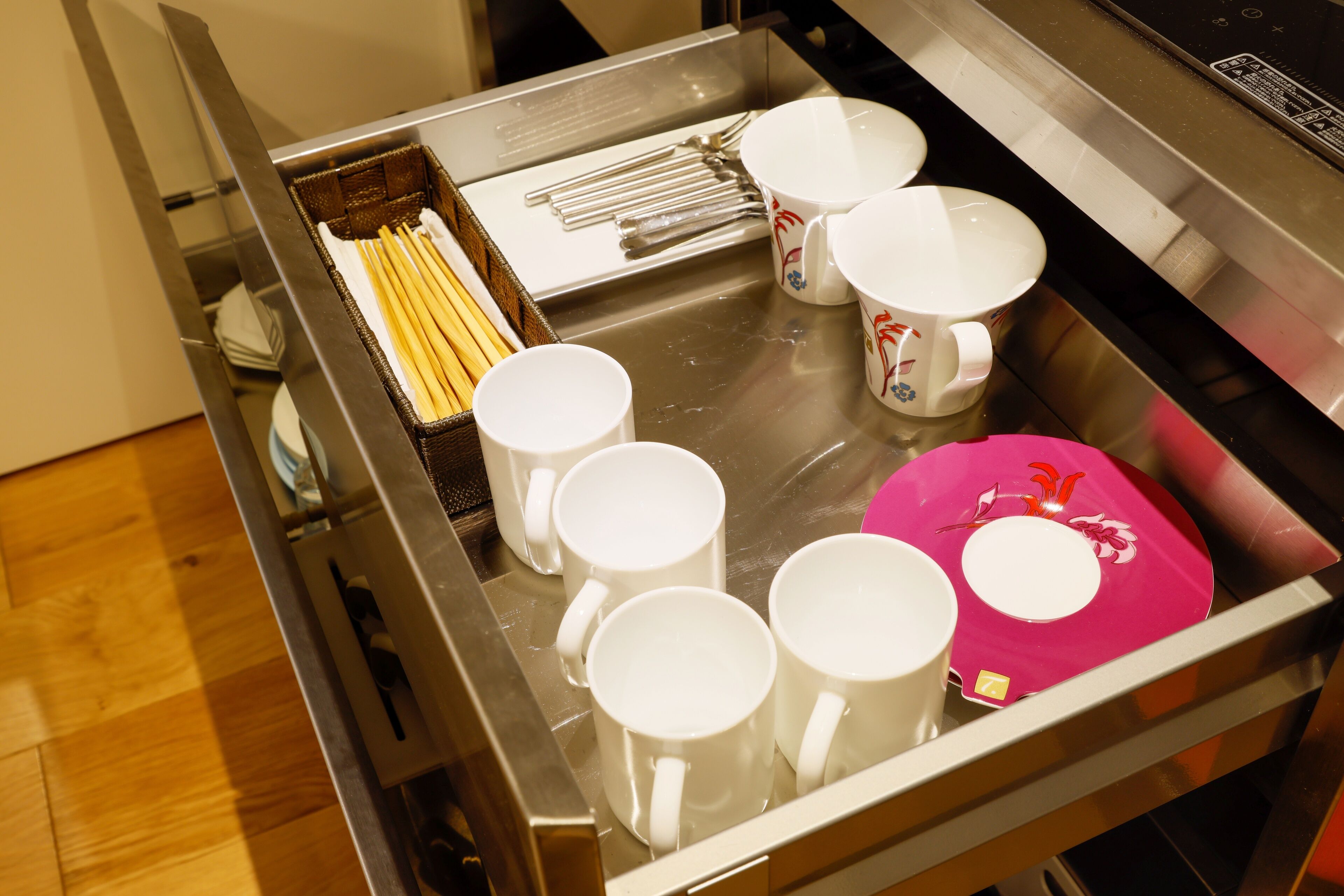 A stainless steel tray with white mugs, a pink plate, and chopsticks.