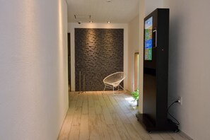 A hallway with a patterned wall, a white chair, and a black cabinet with a screen.