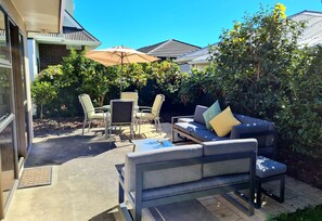 Een terras met een grijze bank, twee stoelen, een kleine tafel en een beige parasol.