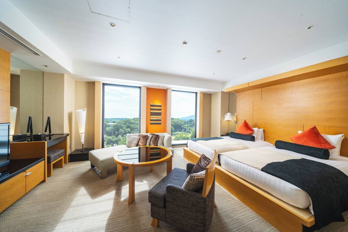 Moderni hotellihuone, jossa on kaksi sänkyä, työpöytä, tuoli ja pieni pöytä.