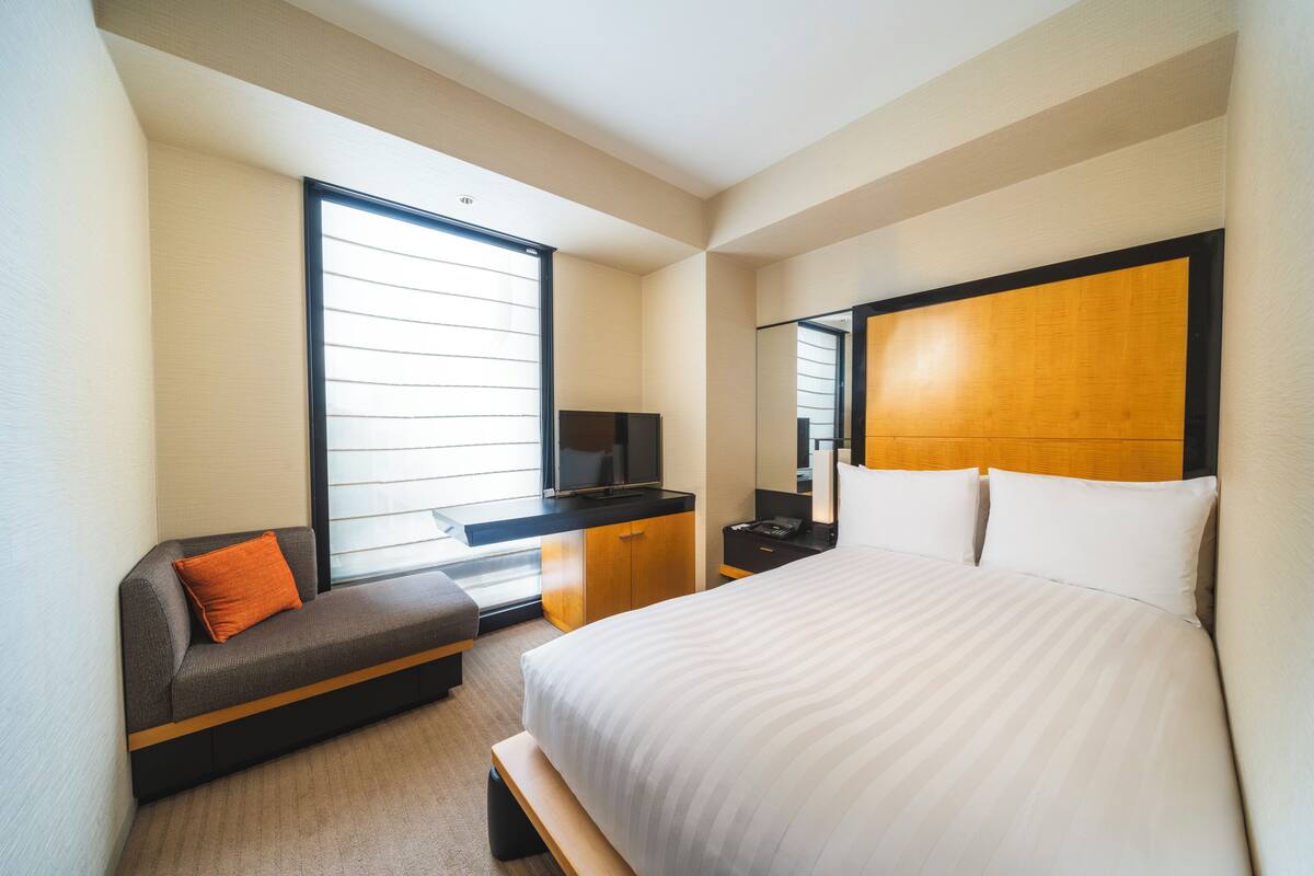 Moderni hotellihuone, jossa on suuri sänky, sohva, kirjoituspöytä, jossa on televisio, ja peili.
