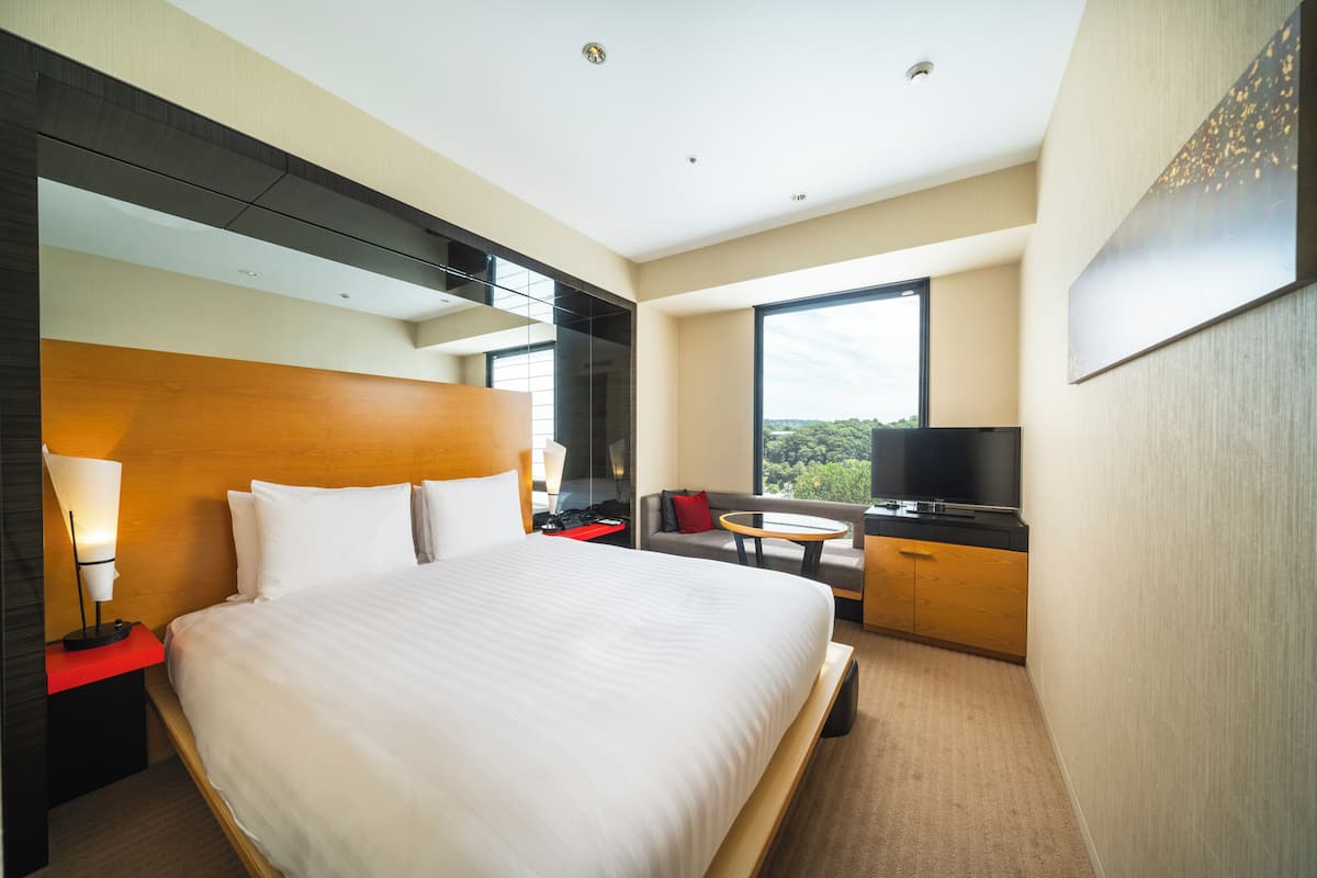 Moderni hotellihuone, jossa on suuri sänky, televisio, sohva ja pieni pöytä.