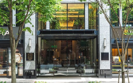 A modern hotel entrance with large glass doors, a clock, and a sign indicating the hotel name.