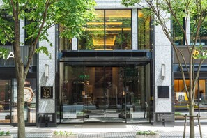 A modern hotel entrance with large glass doors, a clock, and a sign indicating the hotel name.