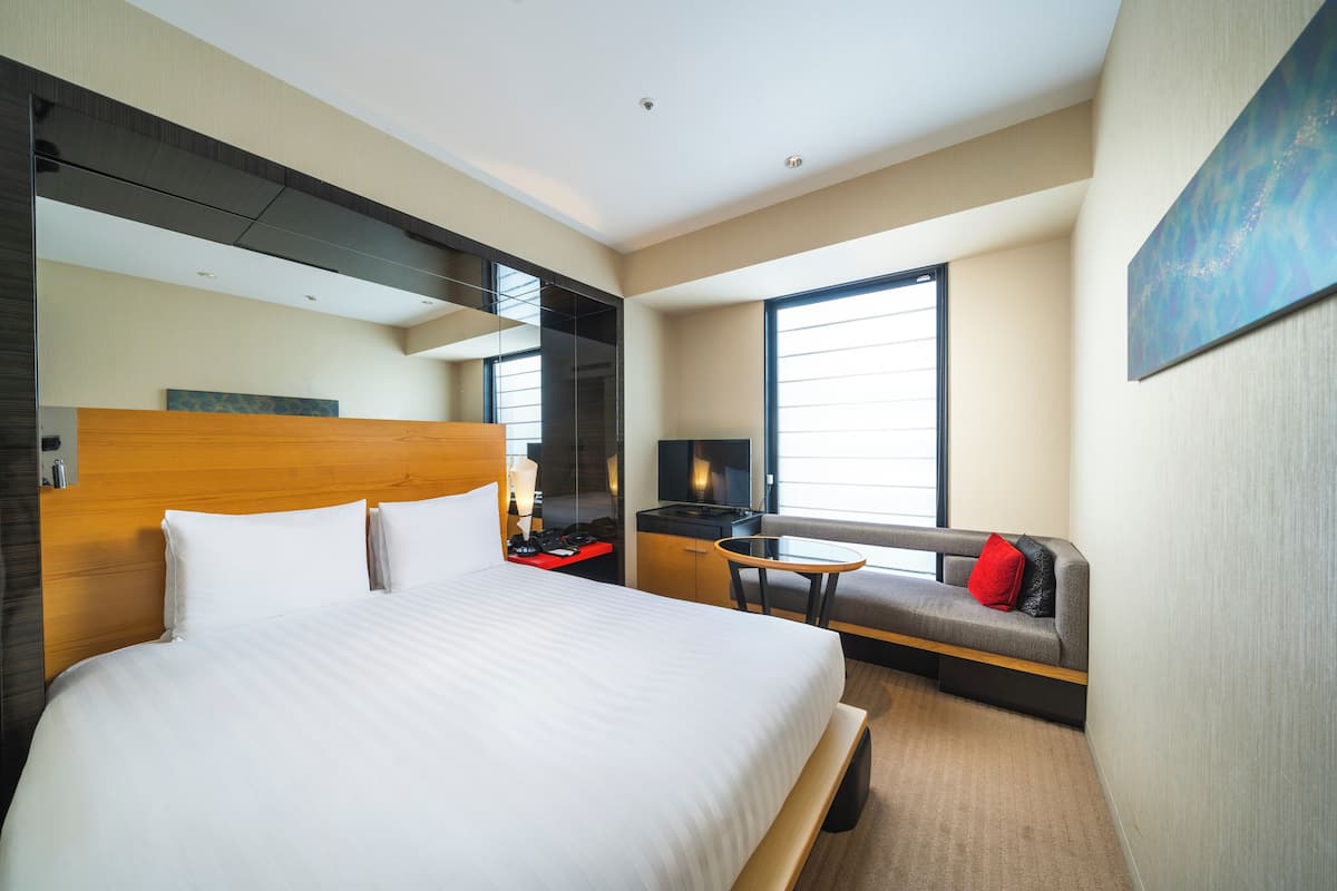 Moderni hotellihuone, jossa on suuri sänky, sohva, työpöytä ja televisio.