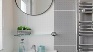 A bathroom with a white sink, a mirror with a decorative frame, a glass shelf with plants, a towel rack, and a toilet. - Room-apple House Wembley - Family Room w (Edgware)