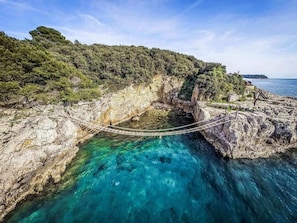 Un puente colgante sobre un mar azul cristalino, con acantilados rocosos y vegetación.