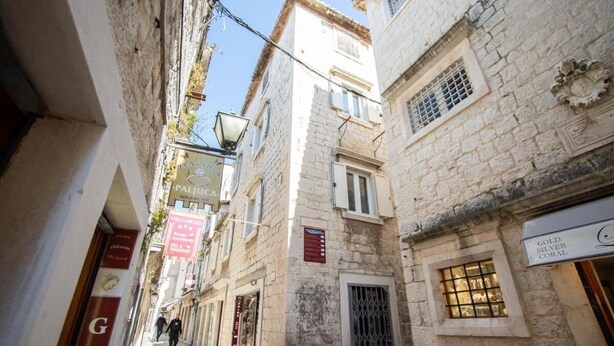 A narrow street with stone buildings, signs for 'Gold Silver Coral' and 'Paliu', and a visible door. - Room-stephane City Vibe Suites - Double (Trogir)