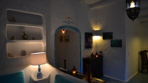 Una habitación acogedora con pared blanca, sofá azul, lámpara, estantes con adornos y una chimenea.