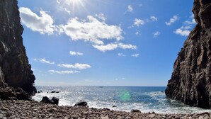 Una playa rocosa con cielo despejado y el sol brillando.