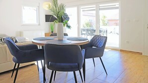 A dining area with a round table, four chairs, a vase with flowers, and a large window with a view. - Basilea Superior Apartment (Malinska-Dubasnica)