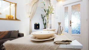 Un coin repas avec une table dressée pour deux personnes, un vase agrémenté de verdure et un miroir décoratif accroché au mur.