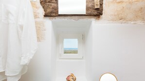 Une salle de bain avec une petite fenêtre, une baignoire blanche, une étagère en bois et une serviette blanche.