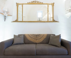 Um sofá marrom com uma manta de renda, um espelho com moldura dourada e um objeto decorativo fixado na parede.