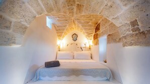 Une chambre confortable aux murs de pierre, avec un lit, des oreillers et une table de chevet.