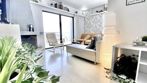 En moderne stue med sofa, sofabord og reol. Der er planter og en lampe.
