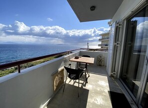 Ein Balkon mit Tisch und Stühlen, der auf ein Gewässer und eine entfernte Küstenlinie blickt.