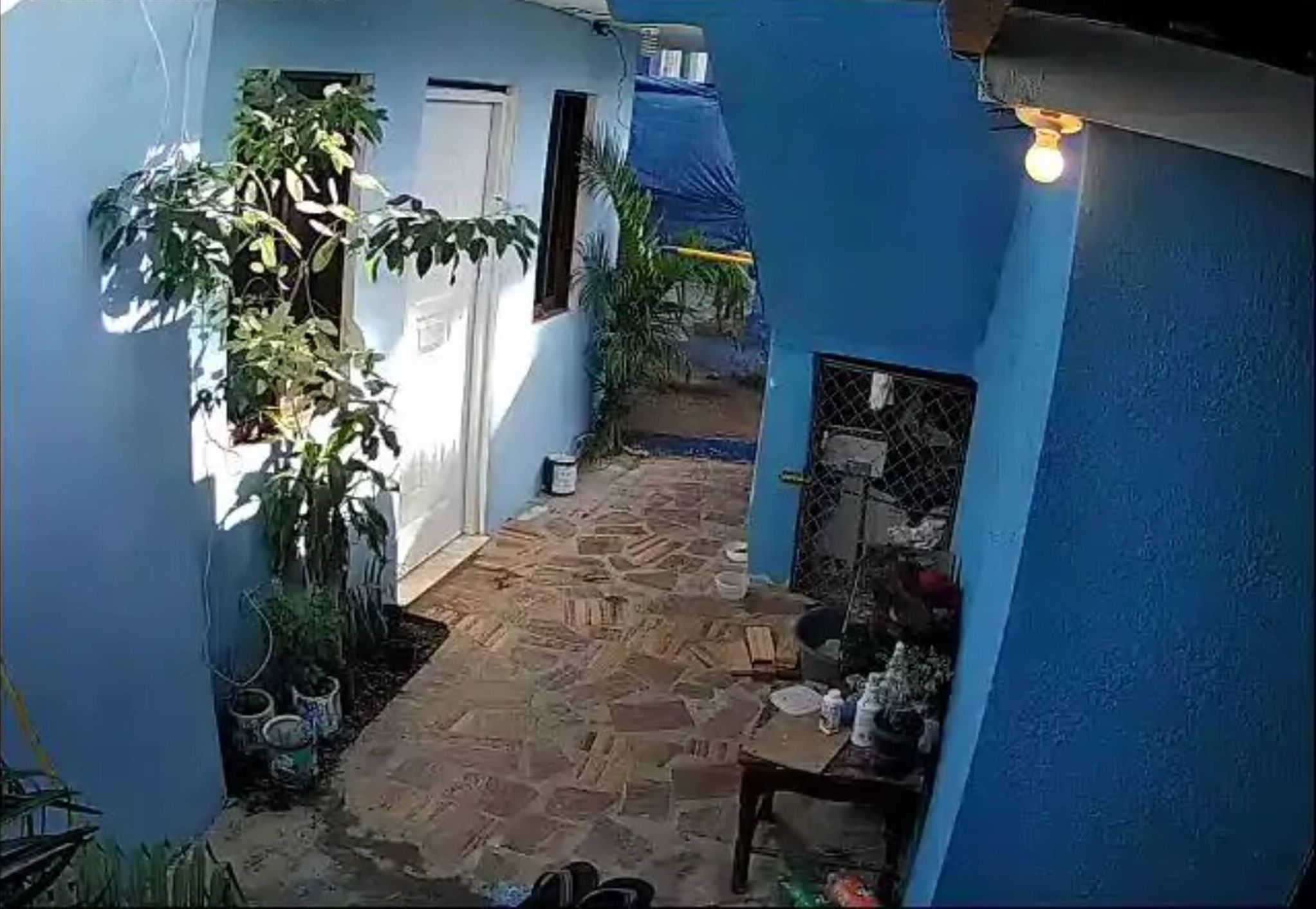 A narrow stone-paved courtyard with a blue wall, a white door, and a small table with items on it.
