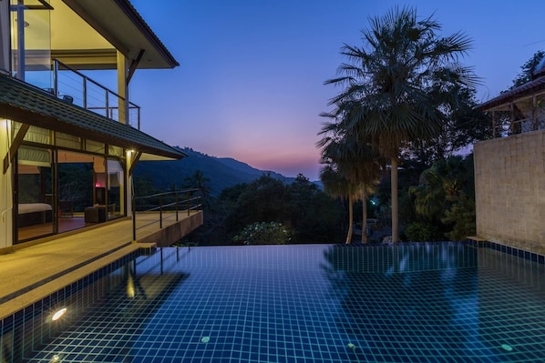 Ett modernt hotell med en stor infinitypool, en balkong med utsikt över bergen och en palm.