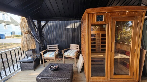 Un espacio al aire libre techado con sauna, dos sillones de mimbre, una mesita con un cuenco y una terraza de madera.