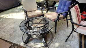Een camping met een metalen tafel en stoelen, een vuurkuil en een caravan.