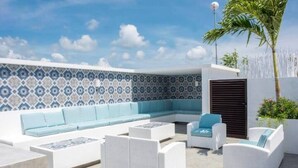 A modern outdoor seating area with a patterned wall, white wicker furniture, and a palm tree. - One Bedroom Penthouse In The Exclusive Aldea Zama (Tulum)