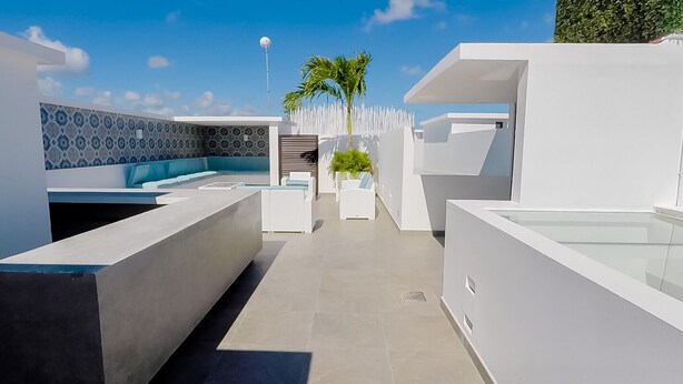 A modern outdoor lounge area with a geometric design, a seating area with a blue cushioned bench, and a palm tree in the background. - One Bedroom Penthouse In The Exclusive Aldea Zama (Tulum)