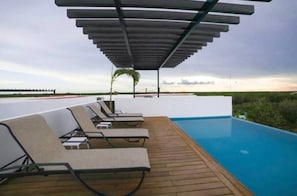 A poolside area with lounge chairs and a pergola. - One Bedroom Penthouse In The Exclusive Aldea Zama (Tulum)