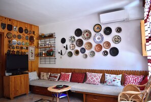 A living room with a wooden wall, a sofa, a television, and a wall of decorative plates.