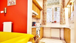 A compact kitchen with wooden cabinets, a microwave, and a window with floral curtains. - Vibrant 3 Bedroom Apartment In The Pulsing Heart Of Budapest (Budapest)