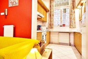 A compact kitchen with wooden cabinets, a microwave, and a window with floral curtains. - Vibrant 3 Bedroom Apartment In The Pulsing Heart Of Budapest (Budapest)