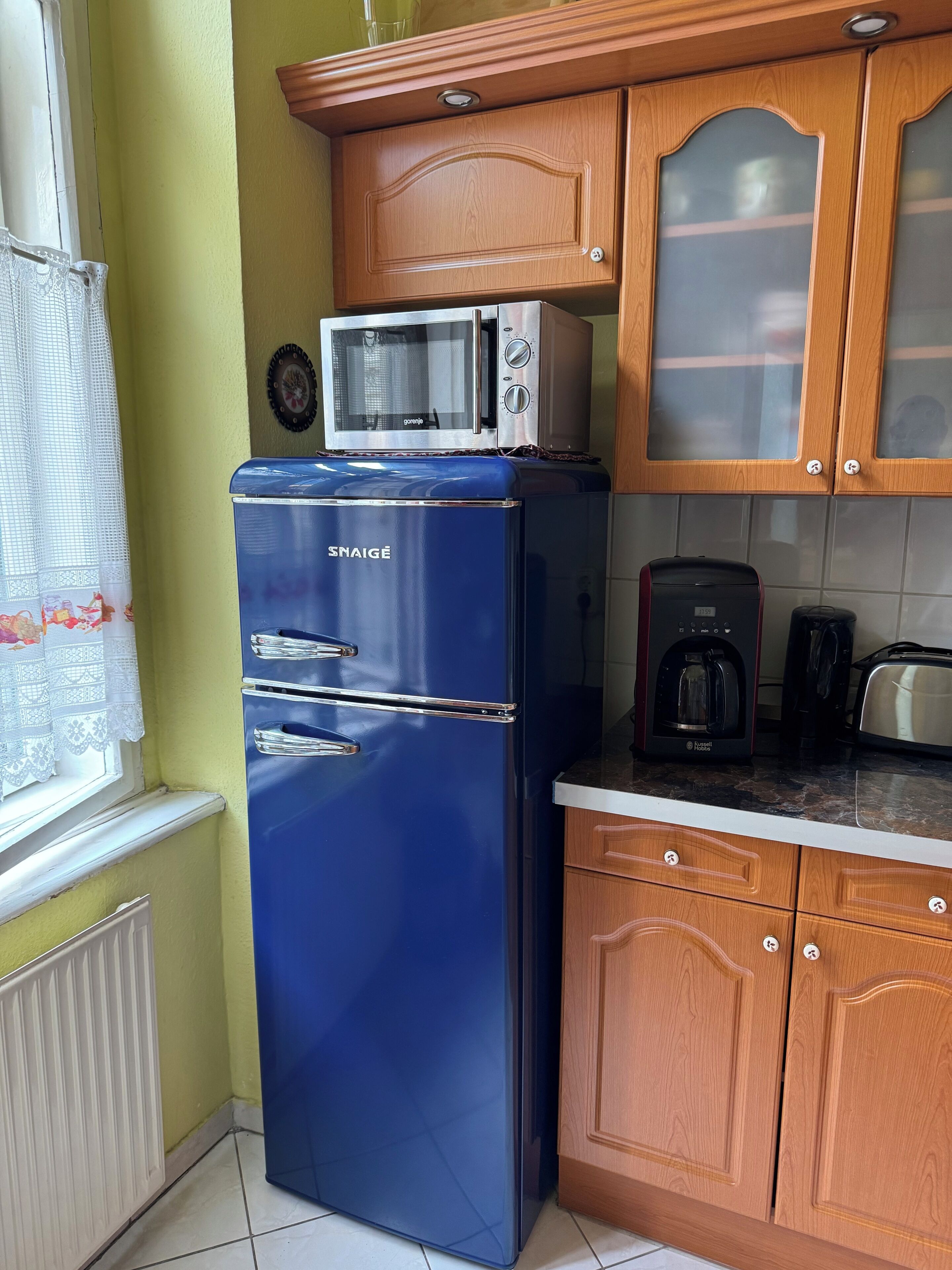 A kitchen with a blue refrigerator, a microwave, and wooden cabinets.