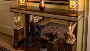 Una consola de madera con un jarrón de flores, dos candelabros encendidos y objetos decorativos, incluyendo una estatua de león y un jarrón con motivos de pájaros.