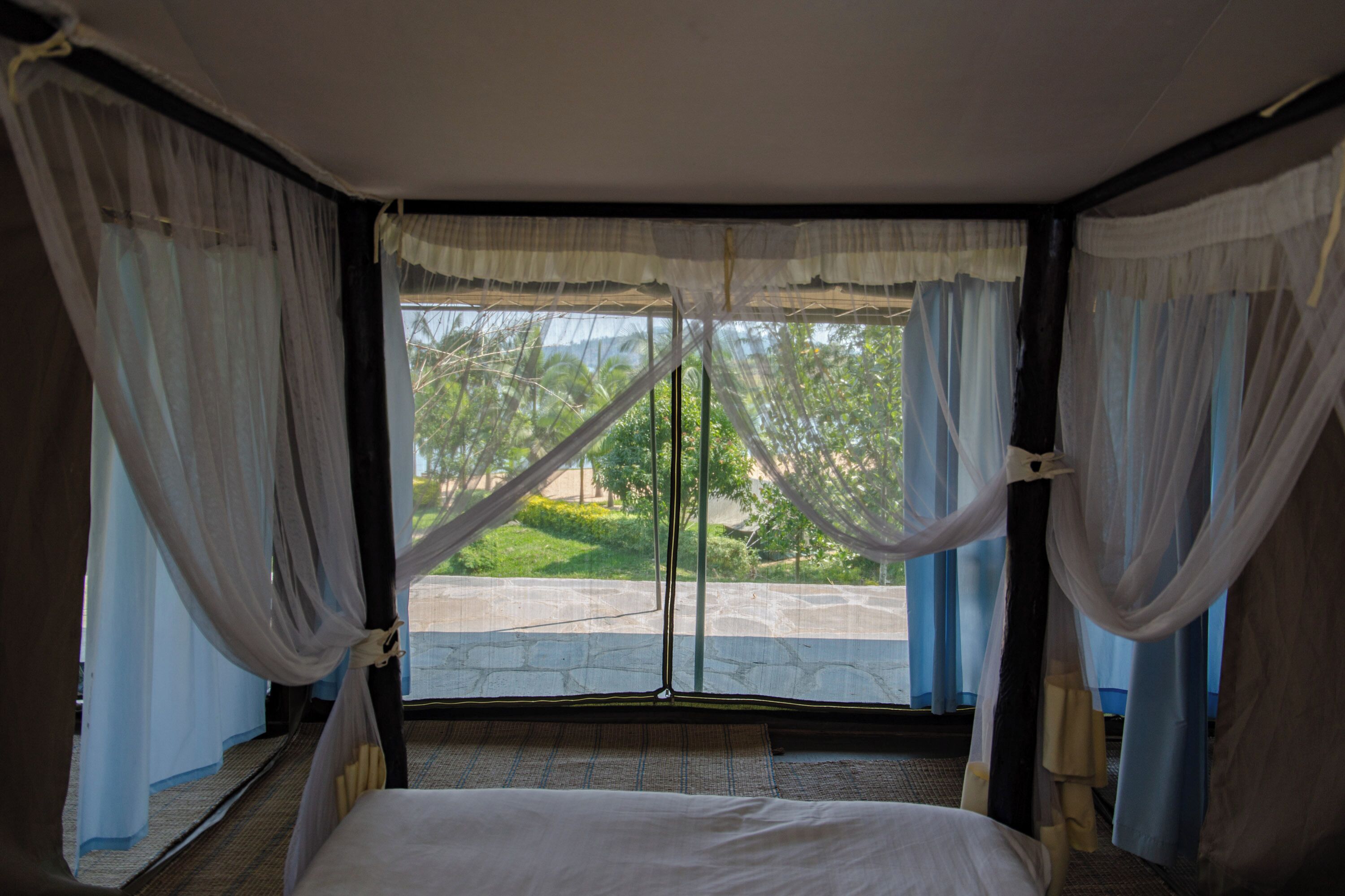 A room with a bed, sheer curtains, and a view of greenery outside.