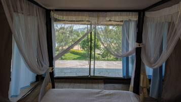 A room with a bed, sheer curtains, and a view of greenery outside.