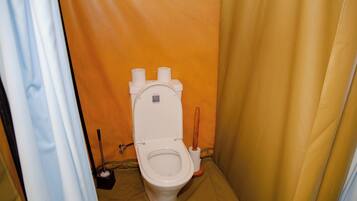 Et lille, lukket badeværelse med toilet, bidét og toiletpapirholder.