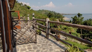 Una escalera de piedra que lleva a un balcón con baranda de madera, con vista a una playa y exuberante vegetación.
