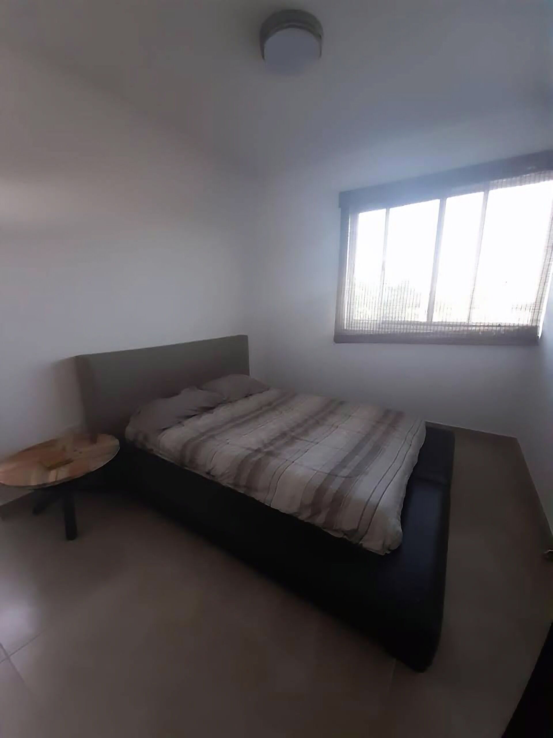 Un dormitorio con una cama, una mesita y una ventana con persianas.